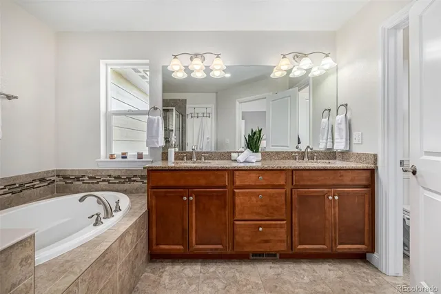 a spacious bathroom with a granite countertop double vanity sink a mirror a window and a bathtub
