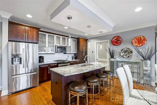 a kitchen with stainless steel appliances granite countertop a refrigerator a stove a sink dishwasher and white cabinets with wooden floor