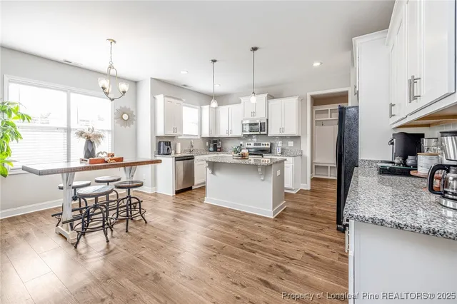a kitchen with stainless steel appliances kitchen island granite countertop a refrigerator a stove a oven and white cabinets with wooden floors