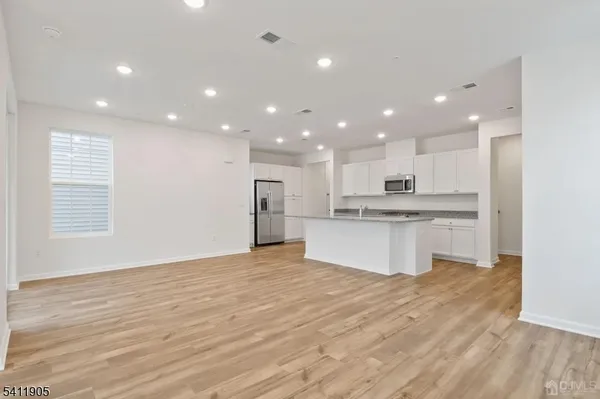 a large kitchen with kitchen island a sink wooden floor white stainless steel appliances and cabinets