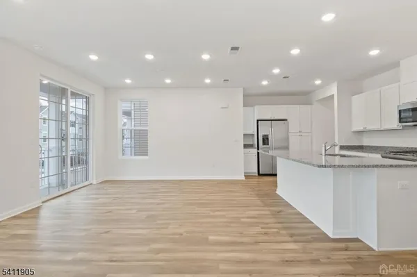 a view of kitchen with kitchen island granite countertop a stove top oven a sink and white cabinets with wooden floor