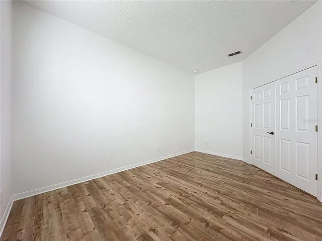 an empty room with wooden floor chandelier fan and windows