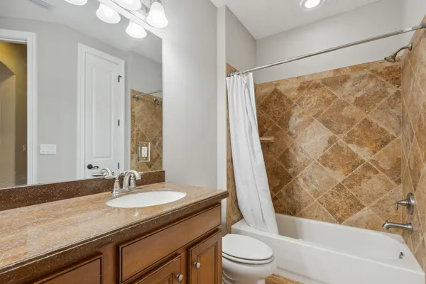 a bathroom with a granite countertop sink a toilet a mirror a bathtub and shower