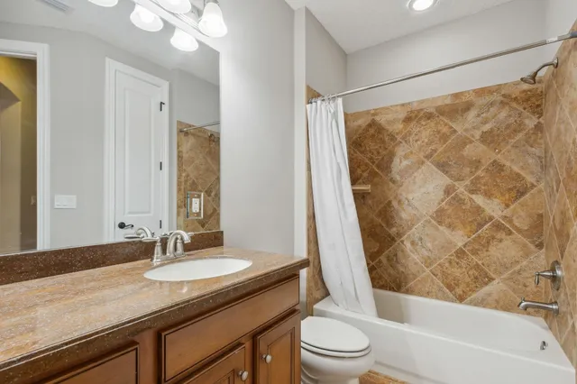 a bathroom with a granite countertop sink a toilet a mirror a bathtub and shower