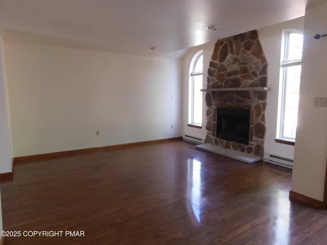 an empty room with wooden floor fireplace and windows