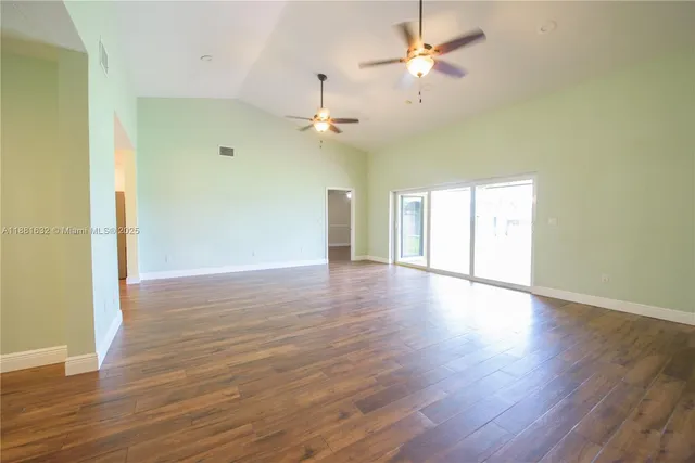 a view of an empty room with wooden floor and a ceiling fan