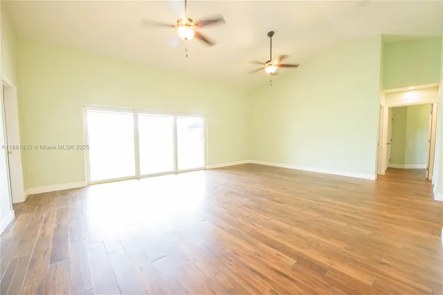 an empty room with wooden floor fan and windows