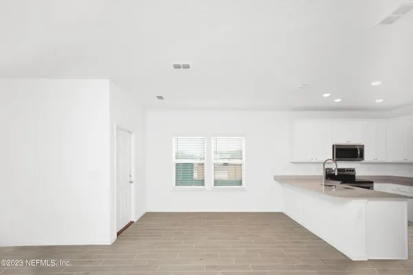 a view of an empty room with kitchen and window