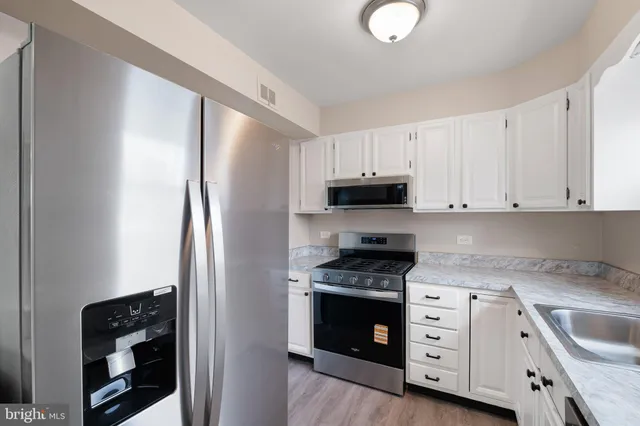 a kitchen with granite countertop a refrigerator stove and white cabinets