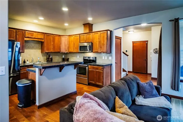 a kitchen with stainless steel appliances granite countertop a refrigerator a sink dishwasher a stove and a dining table with wooden cabinet