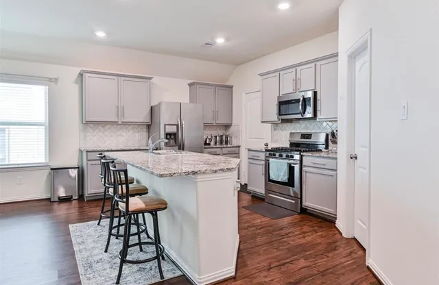 a kitchen with stainless steel appliances kitchen island granite countertop a stove top oven a sink a dining table and chairs with wooden floor