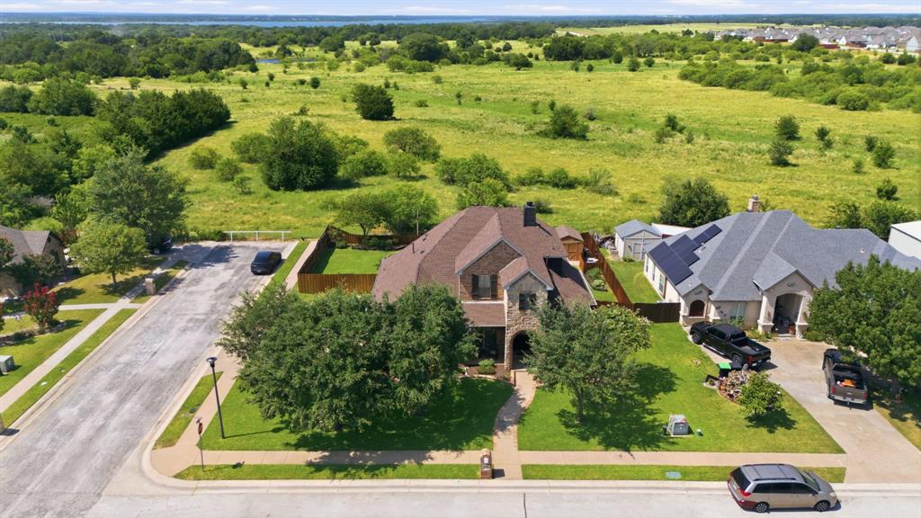 600 Aspen Street Pilot Point, TX 76258 - Photo 35 of 39 Aerial perspective showcasing the residential street, with a prominent brown brick and stone-clad home featuring a multi-gabled roof and mature front yard landscaping
