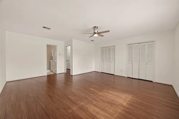 a view of an empty room with wooden floor and a ceiling fan