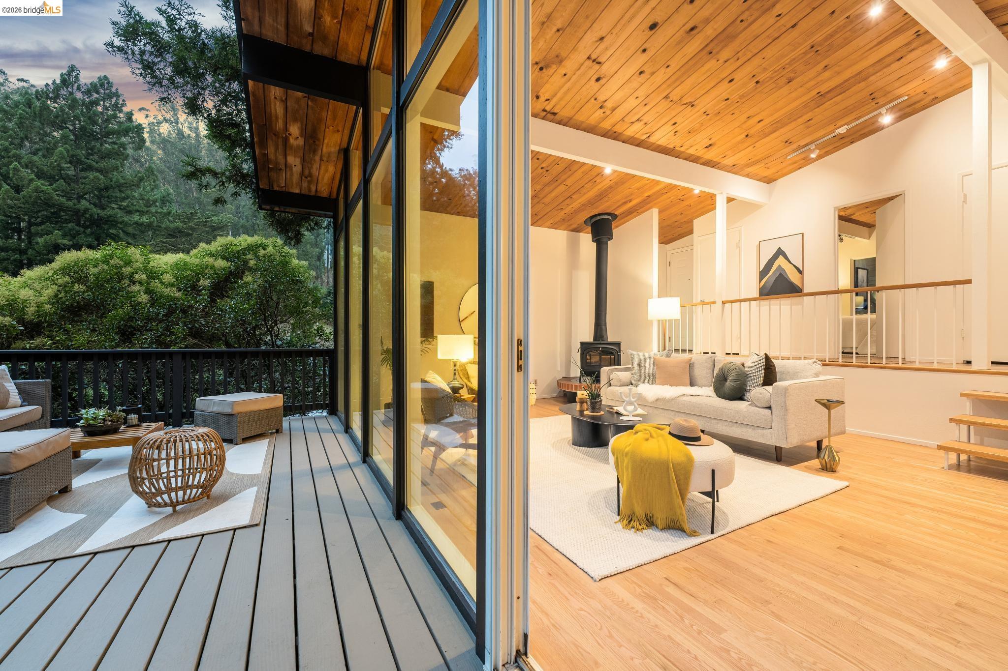 6645 Heather Ridge Way Oakland, CA 94611 - Photo 38 of 61 Spacious deck with composite decking and dark railings, featuring large sliding glass doors opening to a living area with a vaulted wood-paneled ceiling, light wood-finish flooring, and a freestanding wood-burning stove