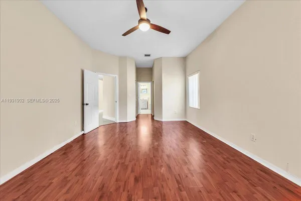 an empty room with wooden floor chandelier fan and windows
