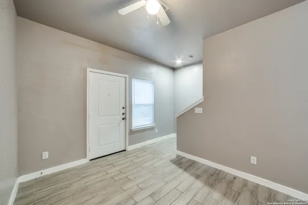 a view of an empty room with wooden floor and a ceiling fan