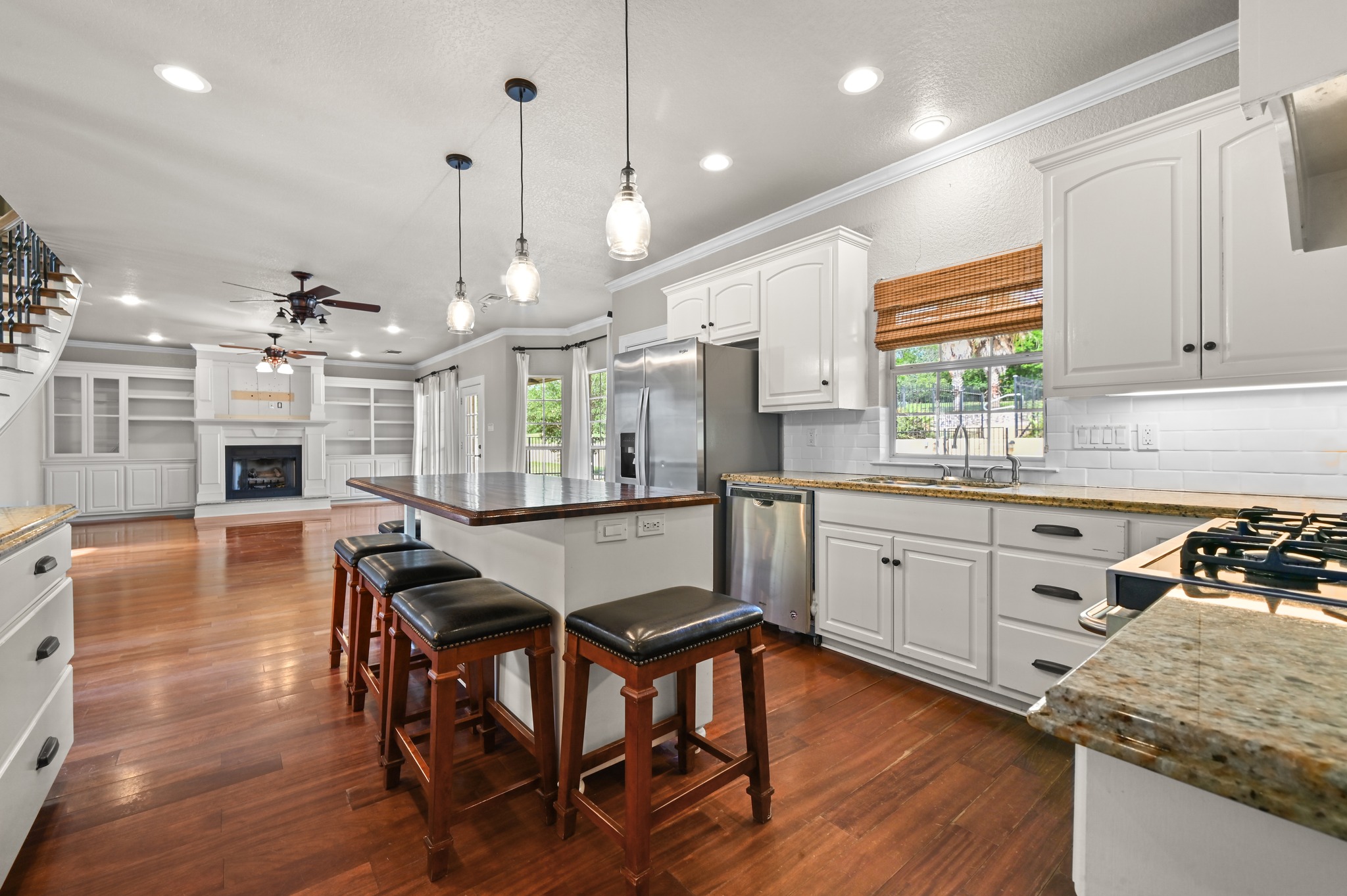 1175 Southern Way Luling, TX 78648 - Photo 23 of 40 Prepare meals in a kitchen featuring granite counters and hardwood floors, with views of the living area's fireplace and built-in shelving.