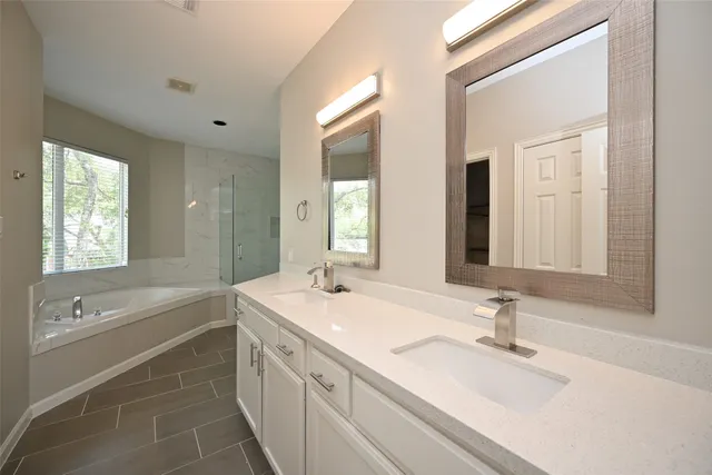 a bathroom with a double vanity sink large mirror and a bathtub