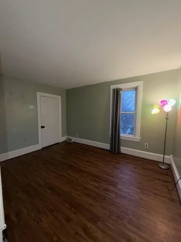 a view of an empty room with wooden floor and window