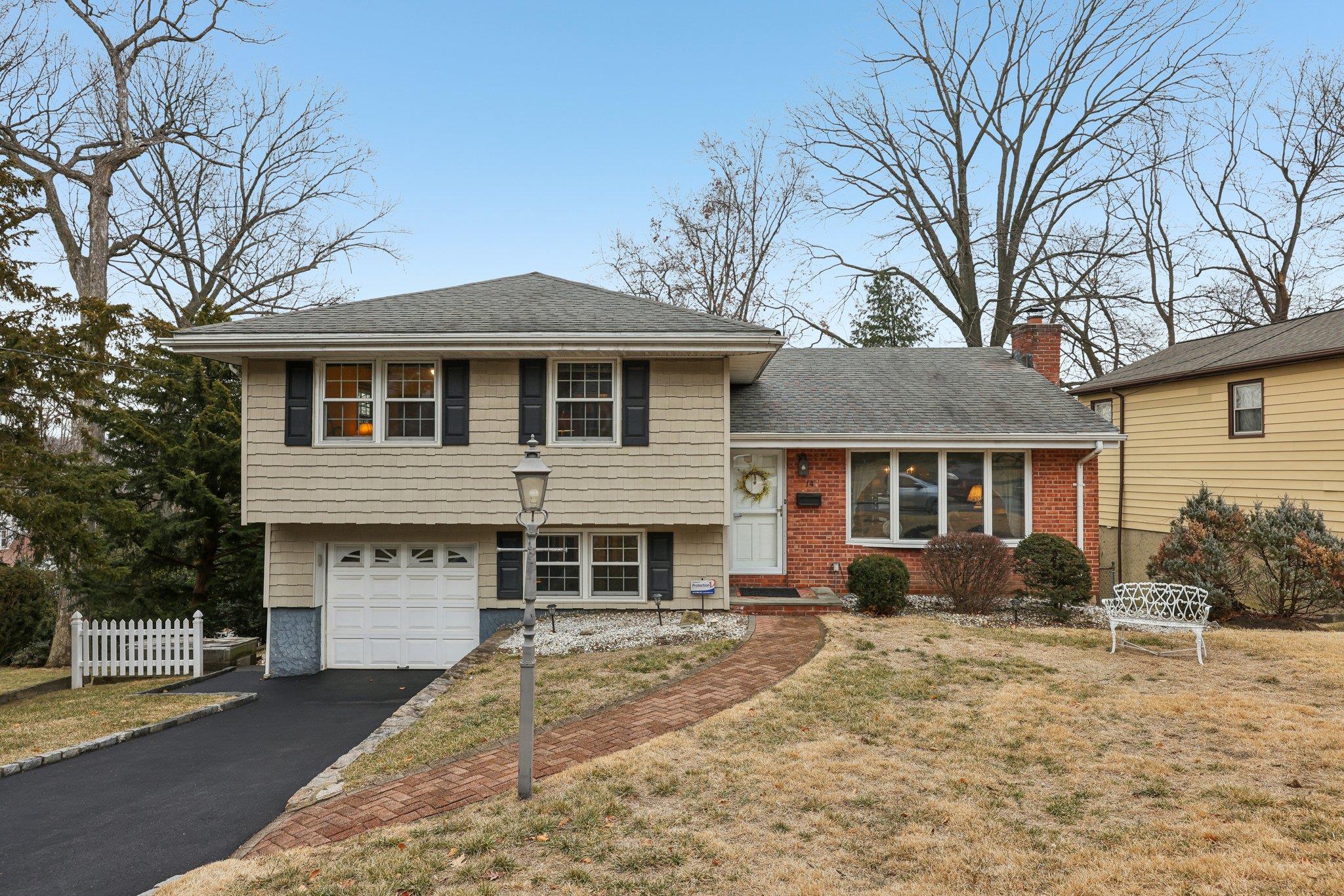 Tri-level home featuring aphalt driveway, a garage, fence, a chimney, and a front yard