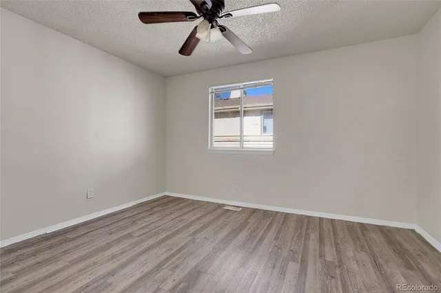 an empty room with wooden floor fan and windows
