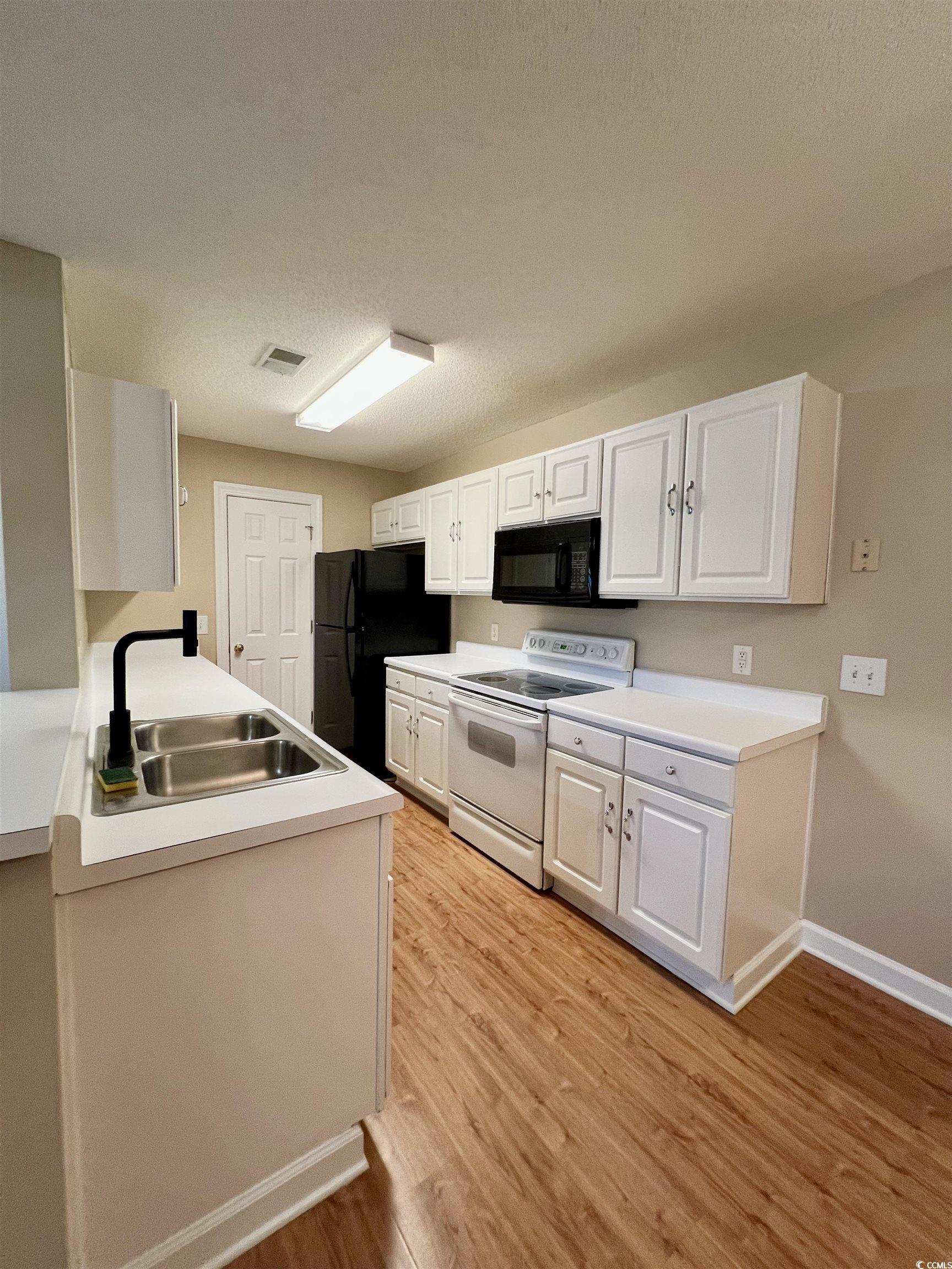 4394 Daphne Lane, Unit F Murrells Inlet, SC 29576 - Photo 6 of 40 Kitchen with black appliances, a sink, light wood-type flooring, white cabinets, and baseboards