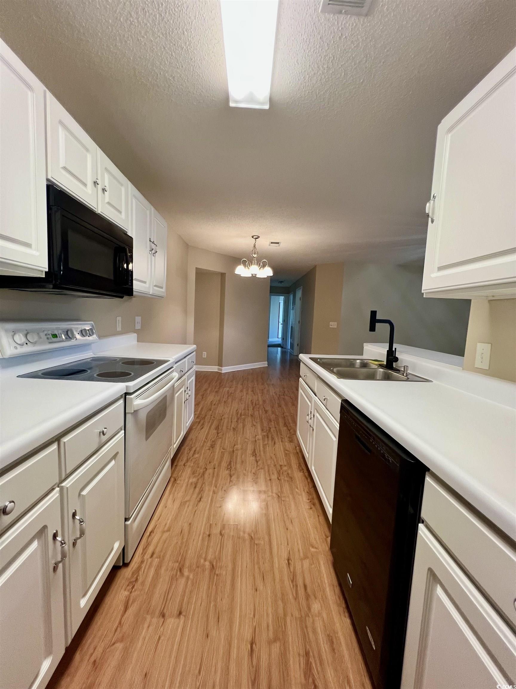 4394 Daphne Lane, Unit F Murrells Inlet, SC 29576 - Photo 9 of 40 Kitchen with black appliances, a sink, light wood-style flooring, white cabinets, and a textured ceiling