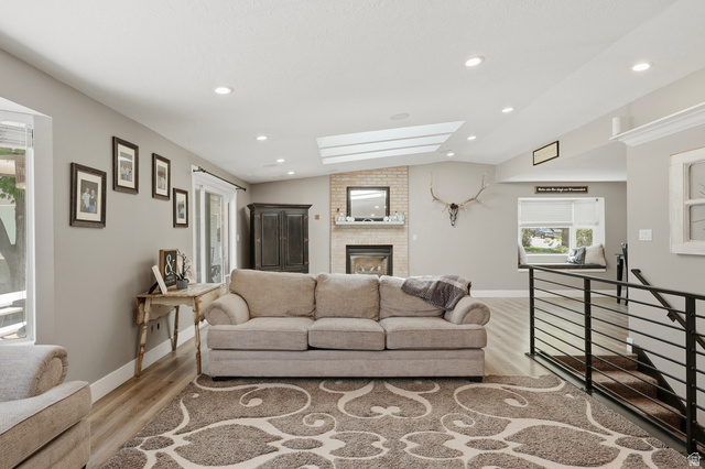 114 North Clark Lane Elk Ridge, UT 84651 - Photo 3 of 26 Spacious living area featuring a brick fireplace with mantel, sloped ceiling with skylights, recessed lighting, and wood-finish flooring