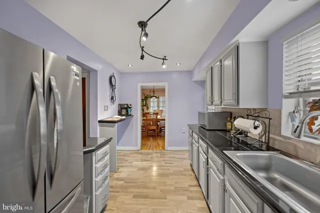 a kitchen with stainless steel appliances granite countertop a refrigerator a sink dishwasher a stove and a dining table with wooden floor