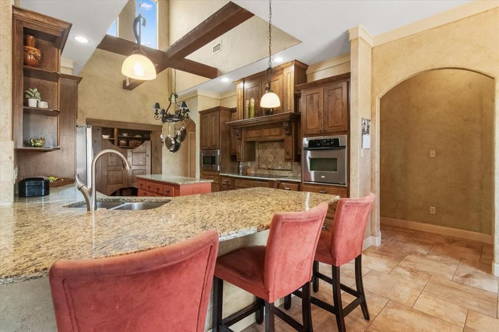 120 Trail Ridge Weatherford, TX 76087 - Photo 19 of 37 Kitchen withbreakfast bar, island, wood cross beams, ceiling is 2 story high. Appliances with stainless steel finishes, Double under counter sinks, open shelves, arched walkways, and light stone countertops