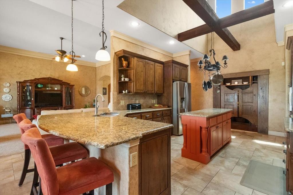 120 Trail Ridge Weatherford, TX 76087 - Photo 20 of 37 Kitchen breakfast bar, iisland, open shelves, island, breakfast bar, pot and pan drawers, pot and pan hanging rack above island, light stone counters, and crown molding