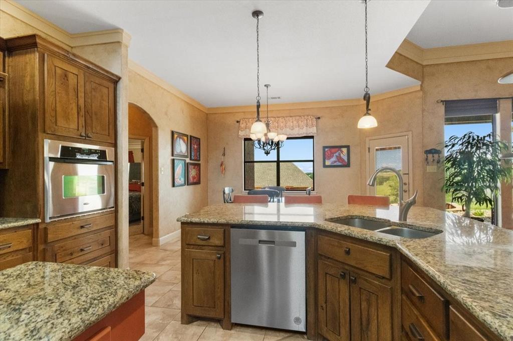 120 Trail Ridge Weatherford, TX 76087 - Photo 23 of 37 Kitchen featuring island, breakfast bar, stainless steel appliances, double under counter sink, brown cabinetry, arched walkways, and open to breakfast area