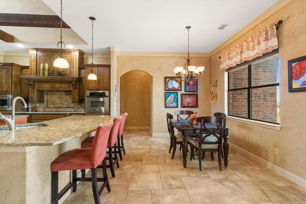 120 Trail Ridge Weatherford, TX 76087 - Photo 25 of 37 Kitchen beakfast bar with a sink, appliances with stainless steel finishes, light stone countertops, decorative backsplash, and a chandelier