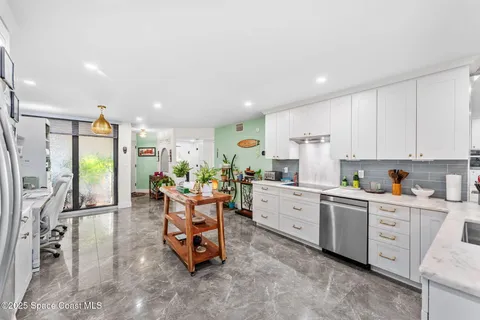a living room with stainless steel appliances furniture a rug and a kitchen view