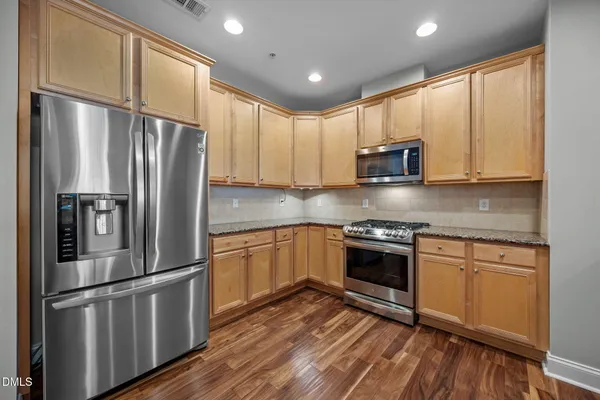 a kitchen with stainless steel appliances granite countertop a refrigerator a stove top oven a sink and dishwasher with wooden floor