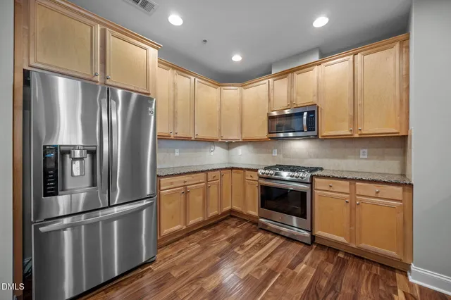 a kitchen with stainless steel appliances granite countertop a refrigerator a stove top oven a sink and dishwasher with wooden floor