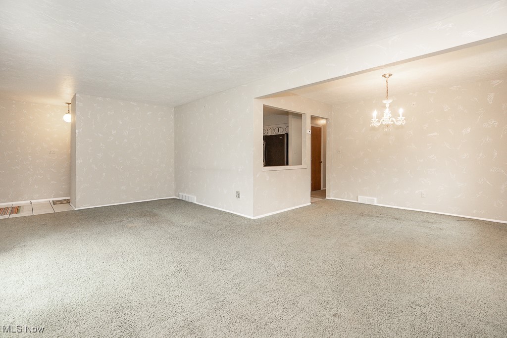 4569 McFarland Road Cleveland, OH 44121 - Photo 9 of 29 Carpeted empty room featuring visible vents, a notable chandelier, and baseboards