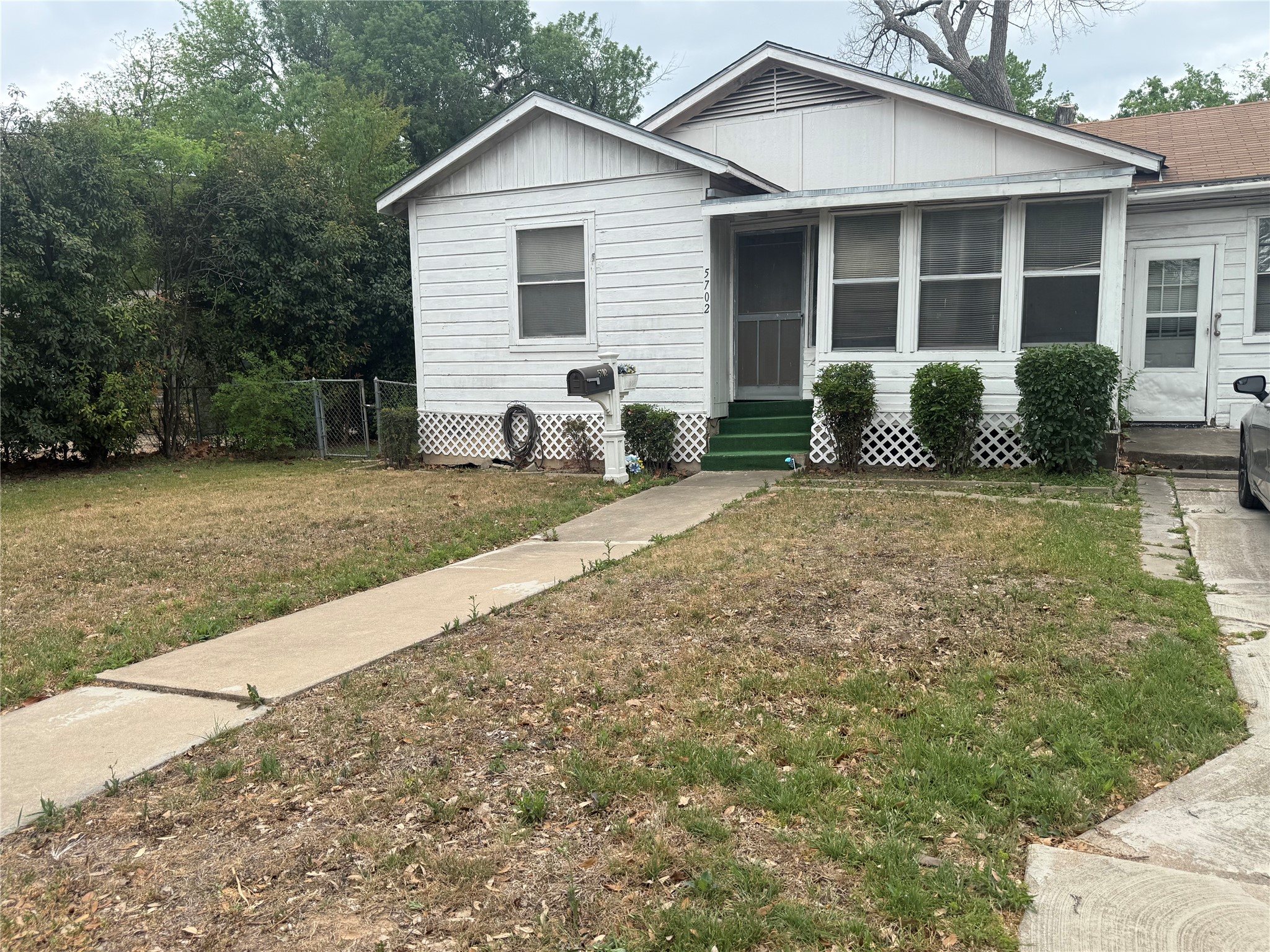 5702 Duval Street Austin, TX 78752 - Photo 2 of 31 White-sided exterior featuring a covered porch with green steps, multiple windows, and a partially screened entry