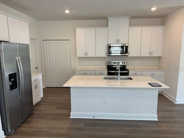 a view of kitchen with stainless steel appliances granite countertop a stove a refrigerator a sink and white cabinets with wooden floor