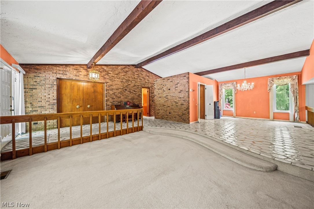 12200 Caves Road Chesterland, OH 44026 - Photo 11 of 43 Carpeted empty room featuring a chandelier, brick wall, and vaulted ceiling with beams