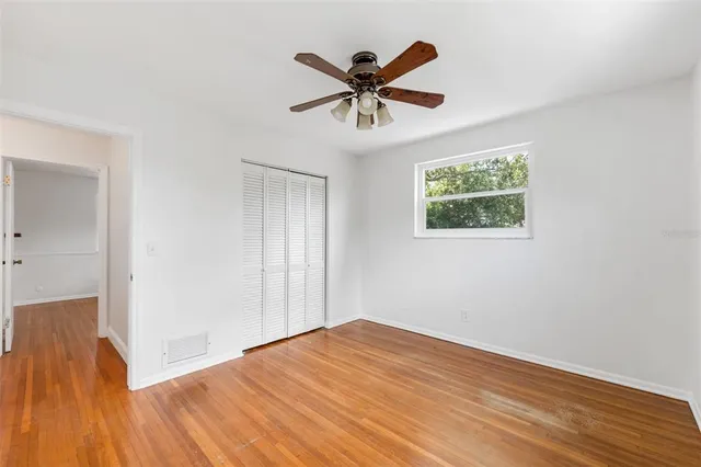 a view of an empty room with wooden floor and a ceiling fan