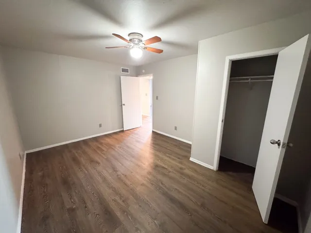 a view of an empty room with wooden floor and a ceiling fan