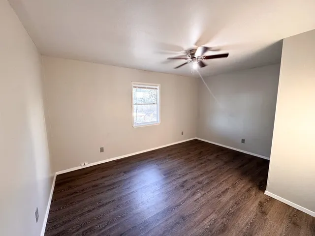 an empty room with wooden floor ceiling fan and windows
