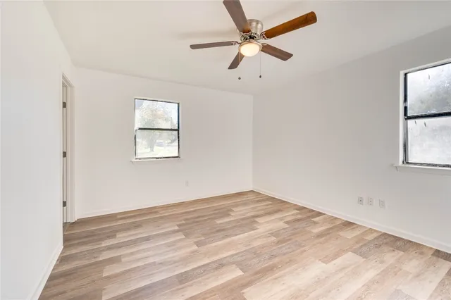 an empty room with wooden floor fan and windows