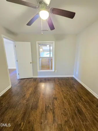 a view of an empty room with wooden floor and a ceiling fan