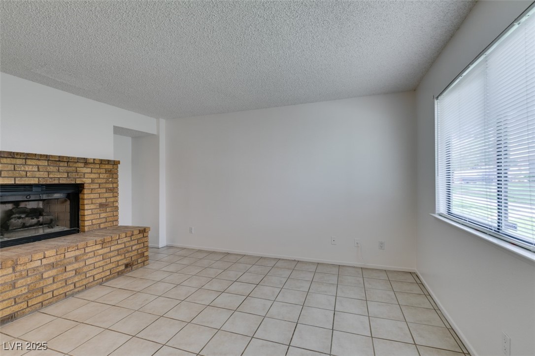 2681 Ruthe Duarte Avenue Las Vegas, NV 89121 - Photo 5 of 43 Unfurnished living room with a fireplace, light tile patterned floors, and a textured ceiling