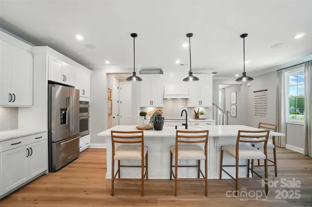 a kitchen with stainless steel appliances kitchen island granite countertop a dining table chairs and a refrigerator