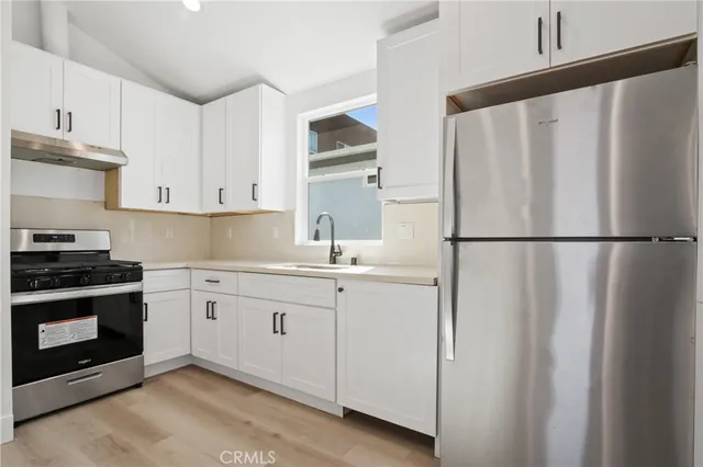 a kitchen with stainless steel appliances granite countertop a refrigerator a sink and white cabinets