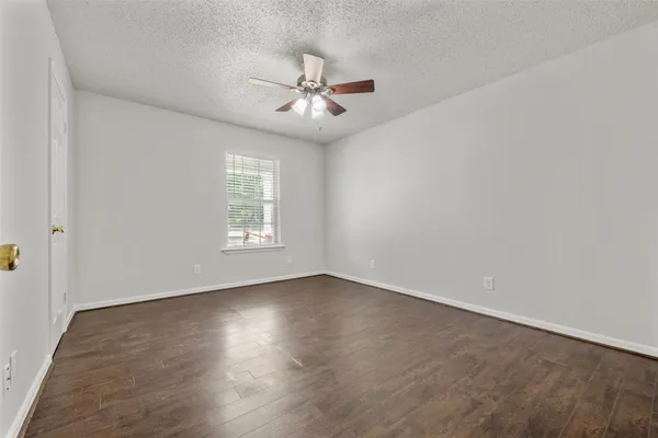 an empty room with wooden floor chandelier fan and windows