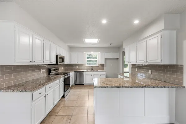 a large kitchen with granite countertop a large counter top space a sink stainless steel appliances and cabinets